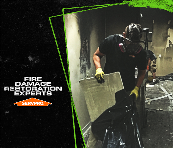 Image of SERVPRO tech wearing a protective face mask while holding sheetrock during fire restoration in a home. 